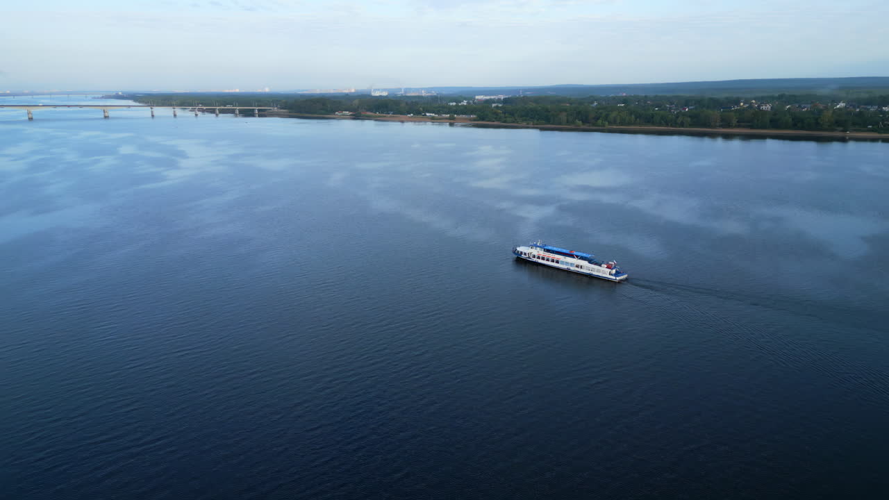 Aerial view of a boat cruising on a wide river with a bridge and city in the background