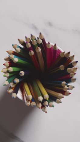 fotografía vertical de lápices multicolores en una olla sobre un fondo de mármol con una persona eligiendo un lápiz rosa