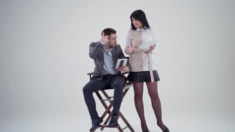 man and woman talking with digital devices. businessman sitting in a chair and explaining something to a beautiful secretary in studio. slow motion.