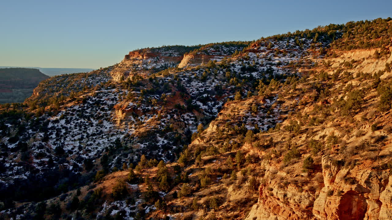 Sweeping drone footage of a multicolored canyon at sunrise, showcasing rugged terrain and sparse vegetation.