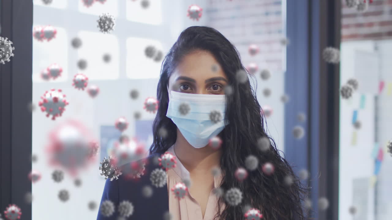 animación de células de covid-19 flotando sobre el retrato de una mujer biracial con máscara facial en la oficina