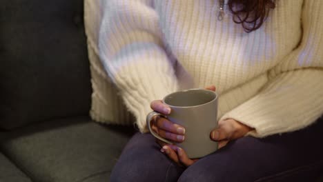 close up of woman of sitting on sofa at home or in bar or coffee shop holding cup of coffee