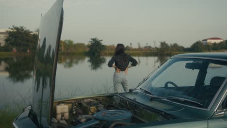 woman by a broken-down vintage car by a lake