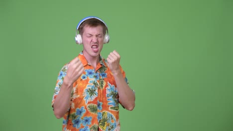 Young tourist man listening to music with young African man looking confused