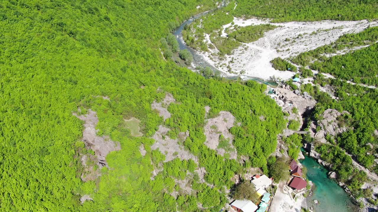 알바니아의 알프스 산맥에서 드론이 녹색 계곡을 날아다니며 푸른 물 강을 가로지르는 다리를 매달고 있습니다.