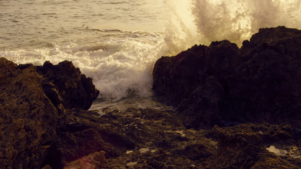 majestuosas olas del océano en cámara lenta chocan contra rocas afiladas durante la hora dorada, ángulo bajo, estático