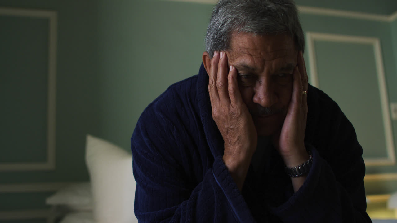 Uomo anziano di etnia mista depresso seduto con la testa tra le mani