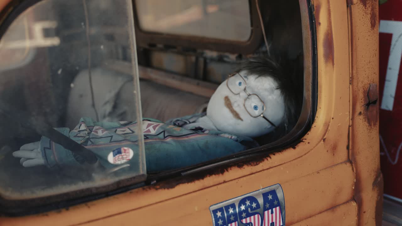 A puppet with glasses in an old wrecked american rusty car.