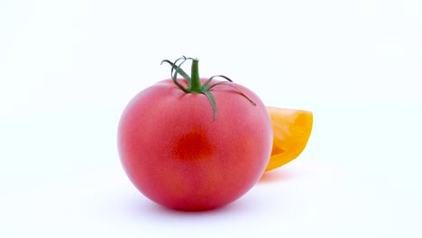 one whole big red tomato and one part of yellow tomato. slowly rotating on the turntable. isolated on the white background. left half of the frame. close-up. macro.