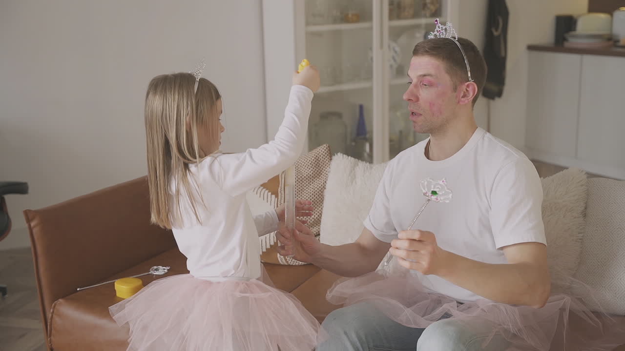 Little Daughter And Her Father Playing With Bubbles Dressed As Princesses And Fairies At Home