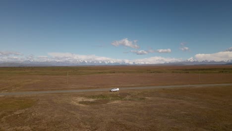 Camino-Vacío-Con-Un-Camión-Averiado-Dentro-De-Un-Paisaje-De-Pradera-Plana,-Montañas-En-Segundo-Plano