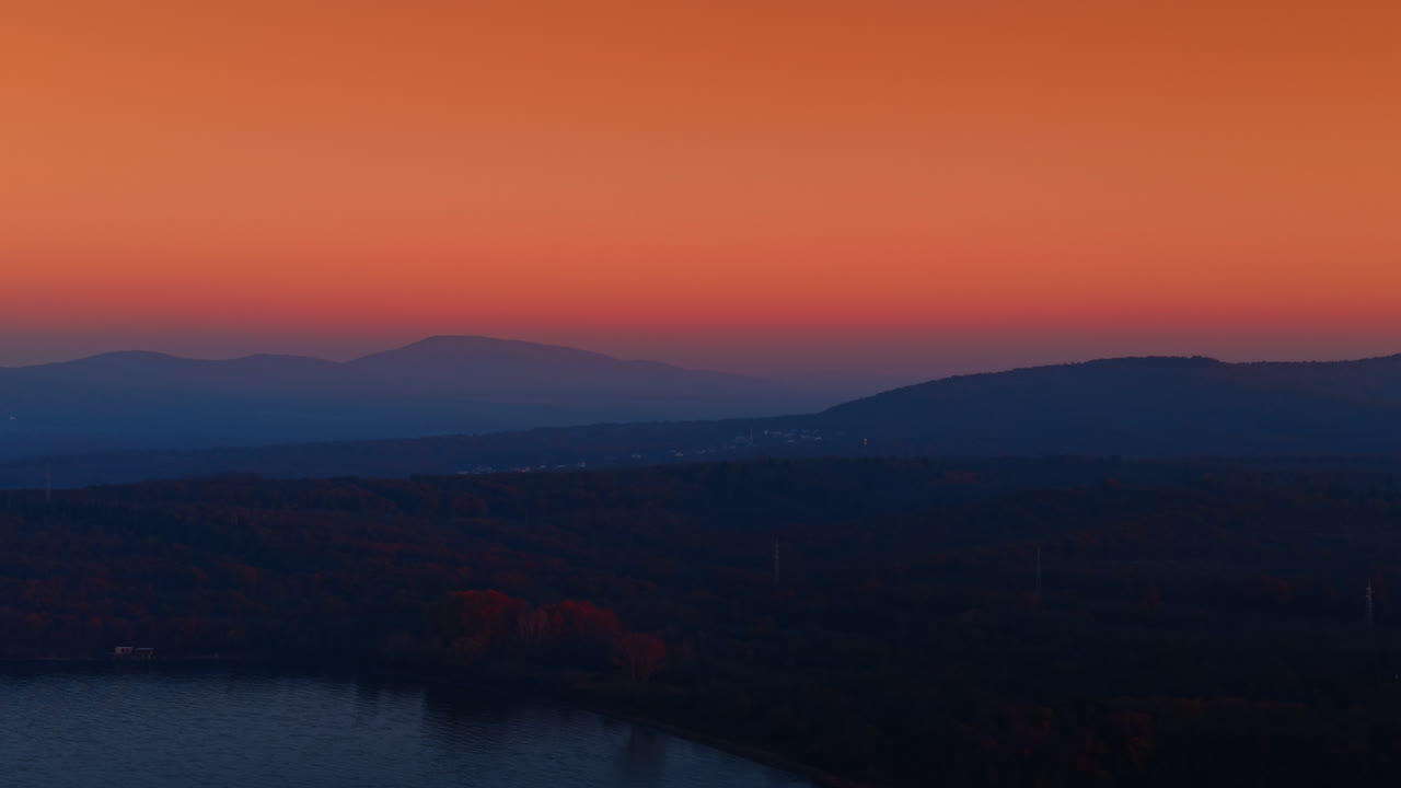 Waterscape, wooded shore and mountains silhouettes. Sunset view of the rocky shore from drone