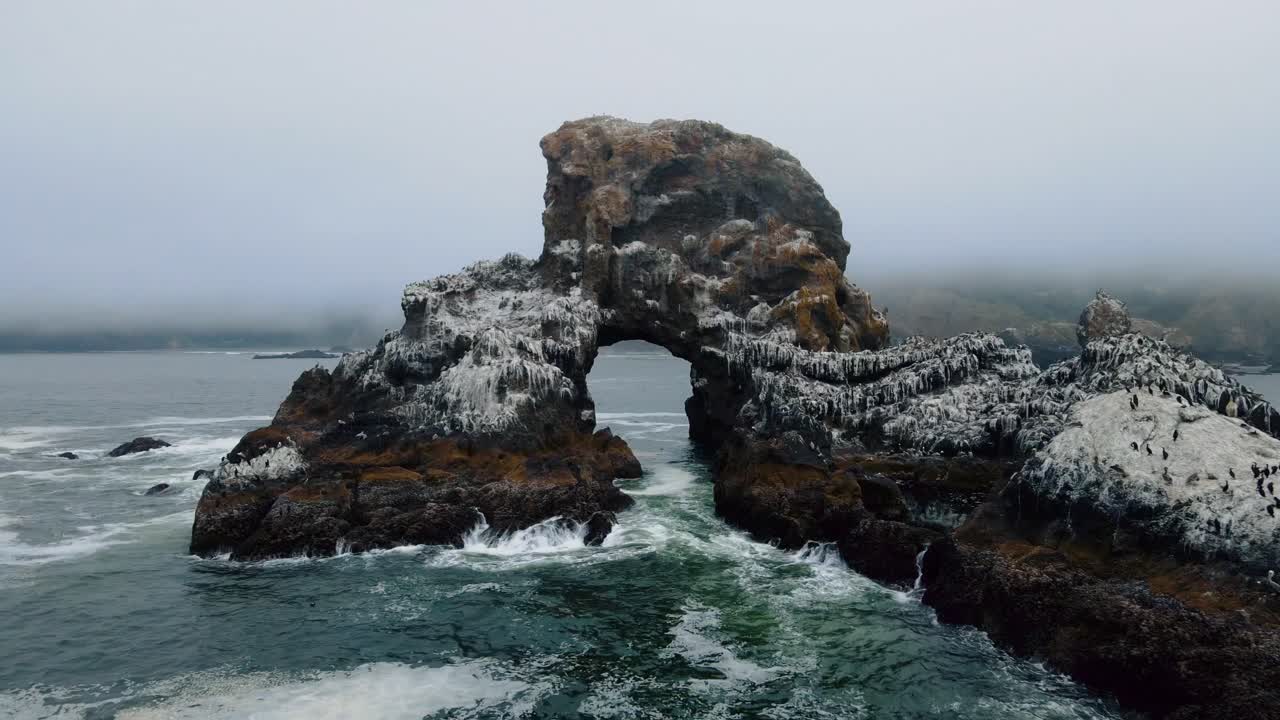 Drone view flying through a rocky cliff formation off the pacific coast at Indian Beach Oregon