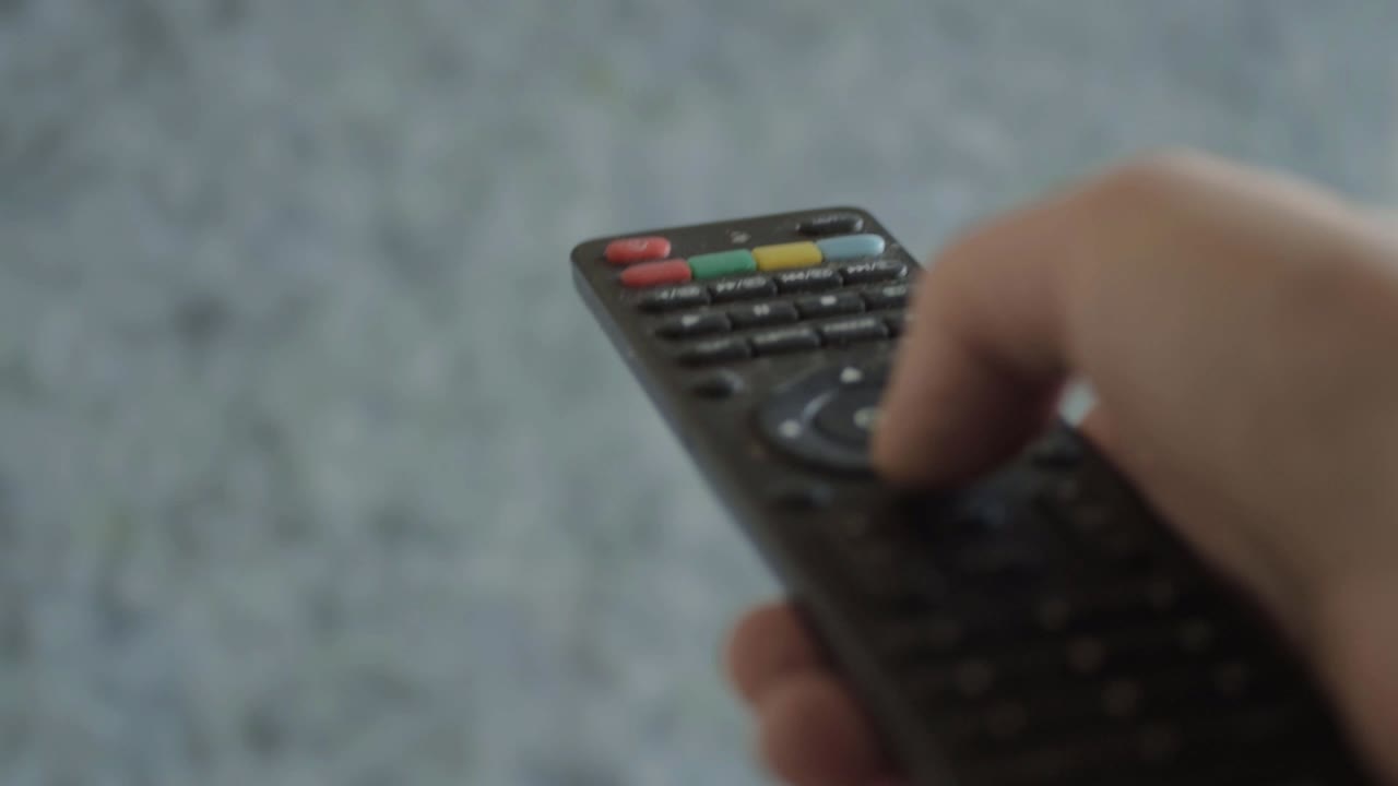 Hand using remote control to change channel with static TV background close up shot