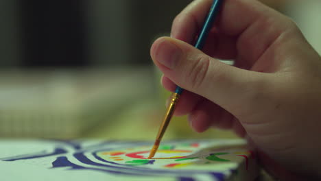 Hand-holding-paintbrush-as-it-paints-on-a-colourful-canvas-Close-up