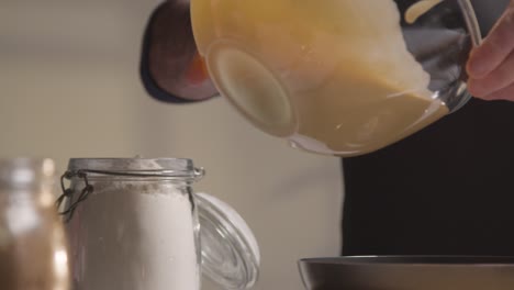 close up of man in kitchen at home pouring mixture into tin to bake cake