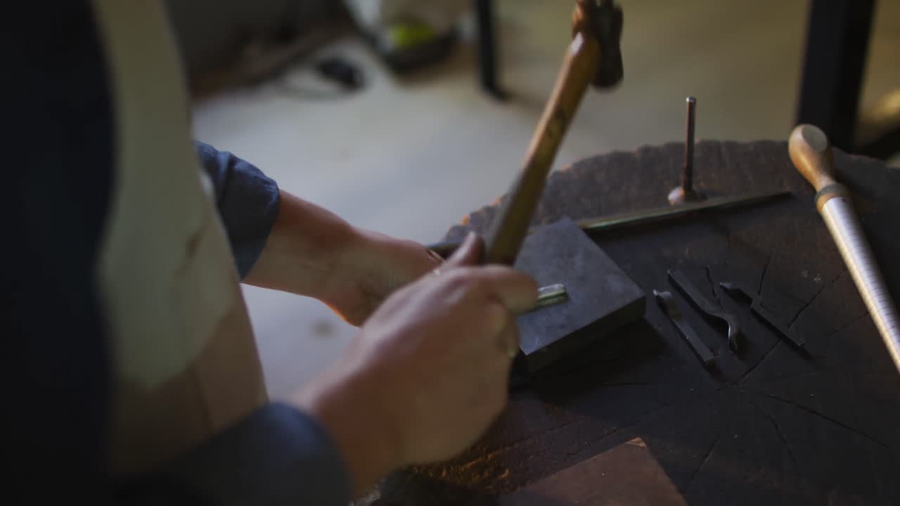 cerca de las manos de una joyera caucásica usando martillo, haciendo joyas