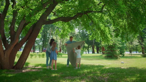 Young-family-picnic-on-lawn-grass.-Parents-preparing-lunch-with-two-children.