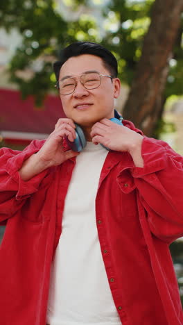 portrait of happy smiling asian man listening music taking off headphones looking at camera outdoors