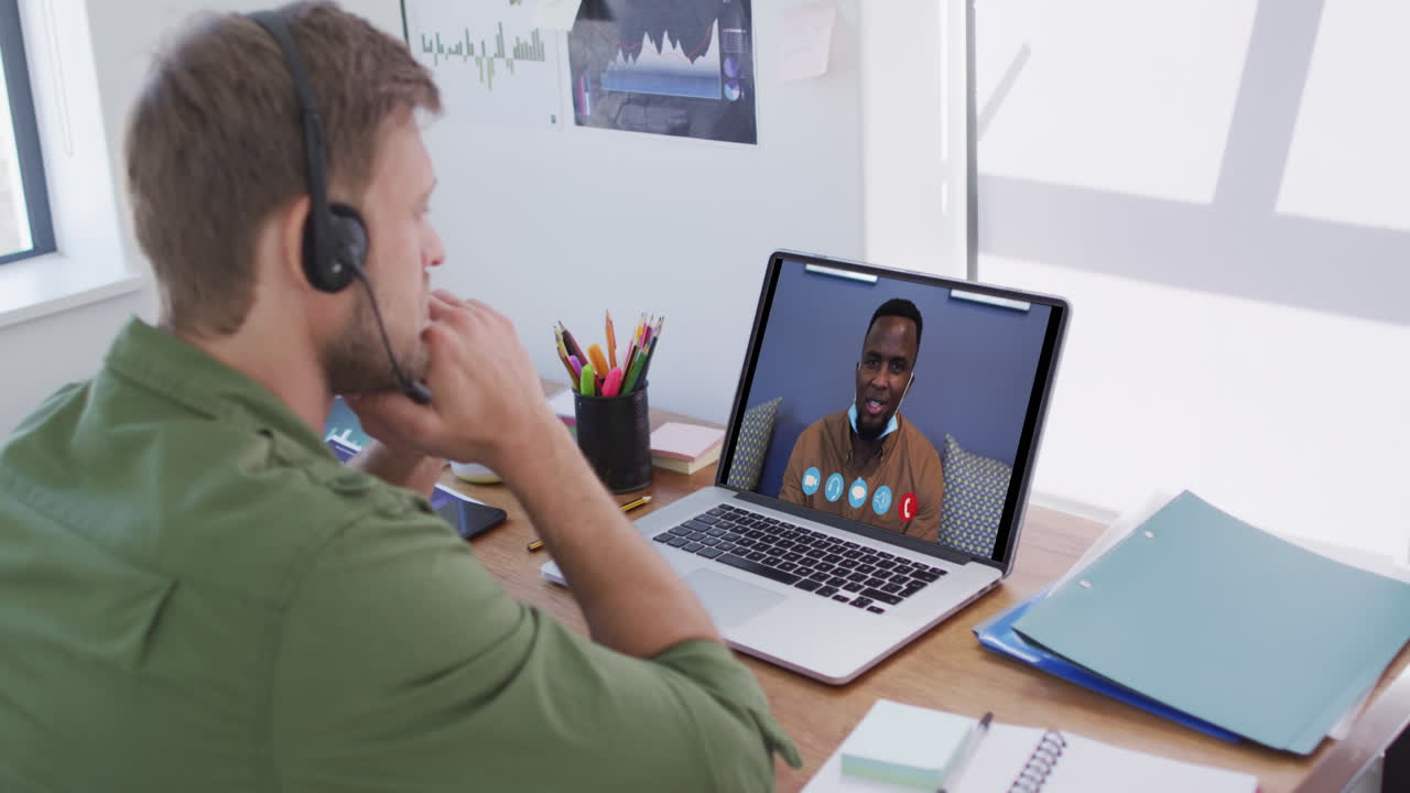 Caucasian man using laptop and phone headset on video call with male colleague