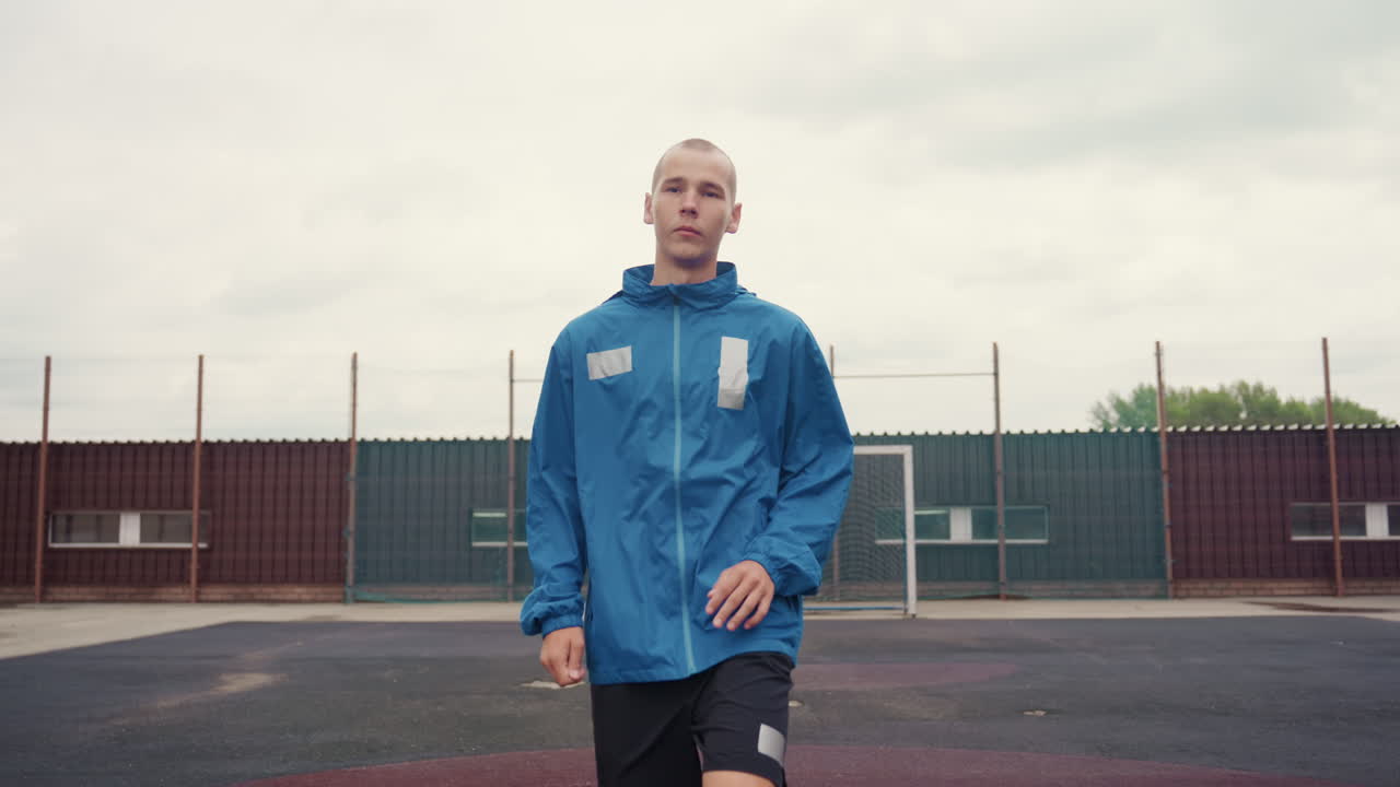 closeup focused white male footballer urban. intimate portrait captures concentrated gaze and controlled footwork on rainswept court, blue jacket and boots visible against city skyline. frames