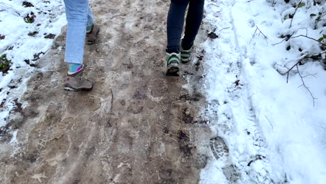 slow motion top down of two women with tramping boots walking on thawed snowy path outdoors during walk in nature