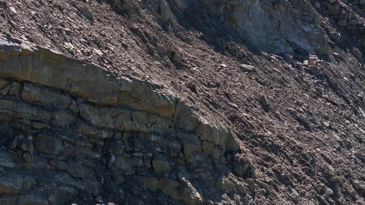 Blottede klippelag og løse sten på den stejle væg i et aktivt stenbrud. Den udgravede skråning afslører geologiske lag, brudt sten og rå mineralforekomster på et industrielt udvindingssted.