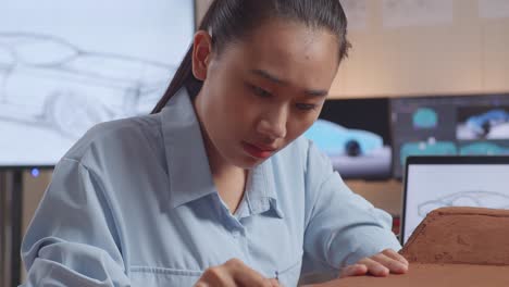 close up of asian woman automotive designer looking at a laptop while working on the sculpture of car clay in the studio