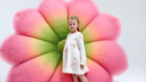 young girl in white dress posing against a giant colorful plush flower