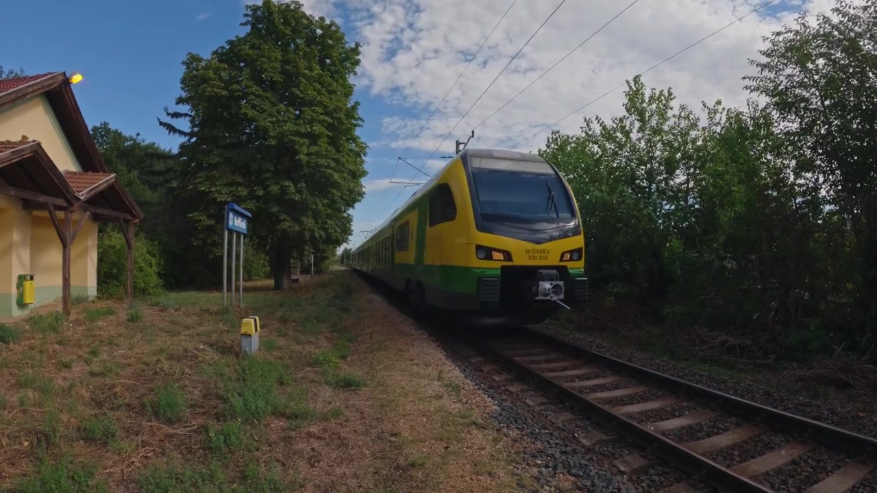 Un moderno treno passeggeri passa una tranquilla stazione ferroviaria rurale su una linea elettrificata.