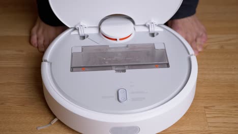 las manos masculinas sacan el recipiente de polvo de la aspiradora robot automática.