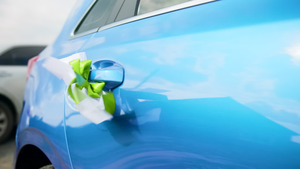 Auto blu decorata con fiocco a nastro verde sulla maniglia della portiera, vernice metallizzata lucida che riflette il cielo, matrimonio festivo