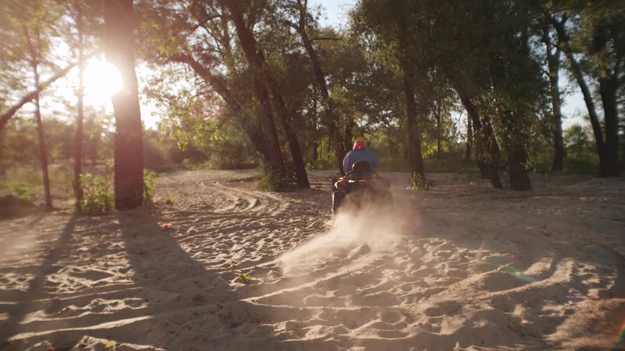 hombre conduciendo un atv en la arena en el bosque al atardecer. hombre conduciendo una bicicleta quad en el parque