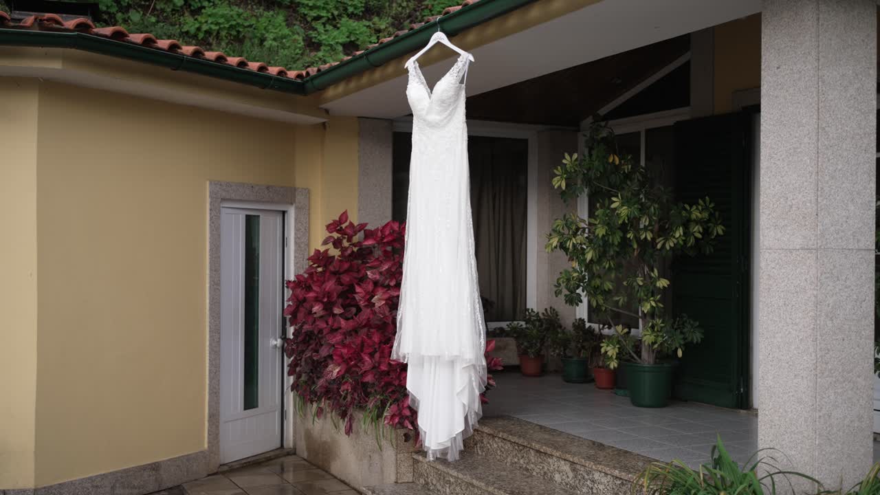white bridal gown hanging under porch roof with potted plants and red leaves in view