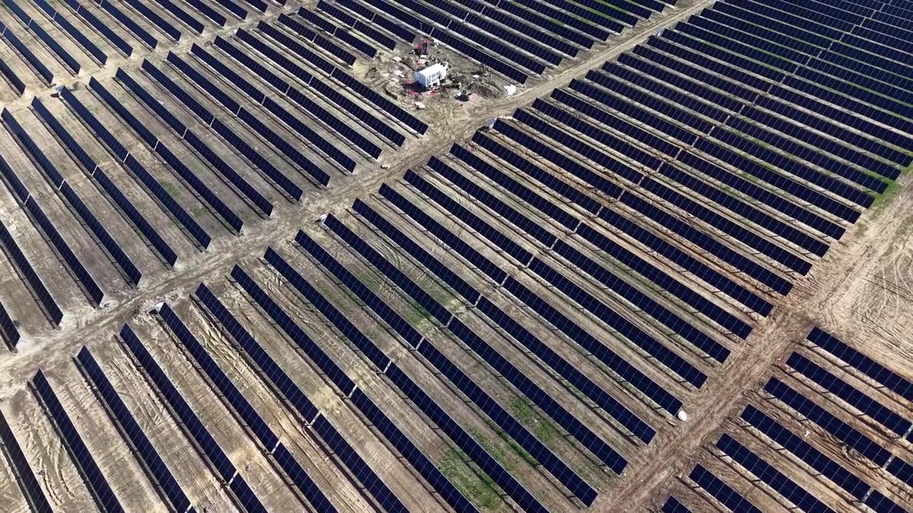 Dronevideo viser en stor solcellepark med ordnede, uendelige rækker af skinnende solcellepaneler i skarpt dagslys, der understreger vedvarende energi og moderne infrastruktur.