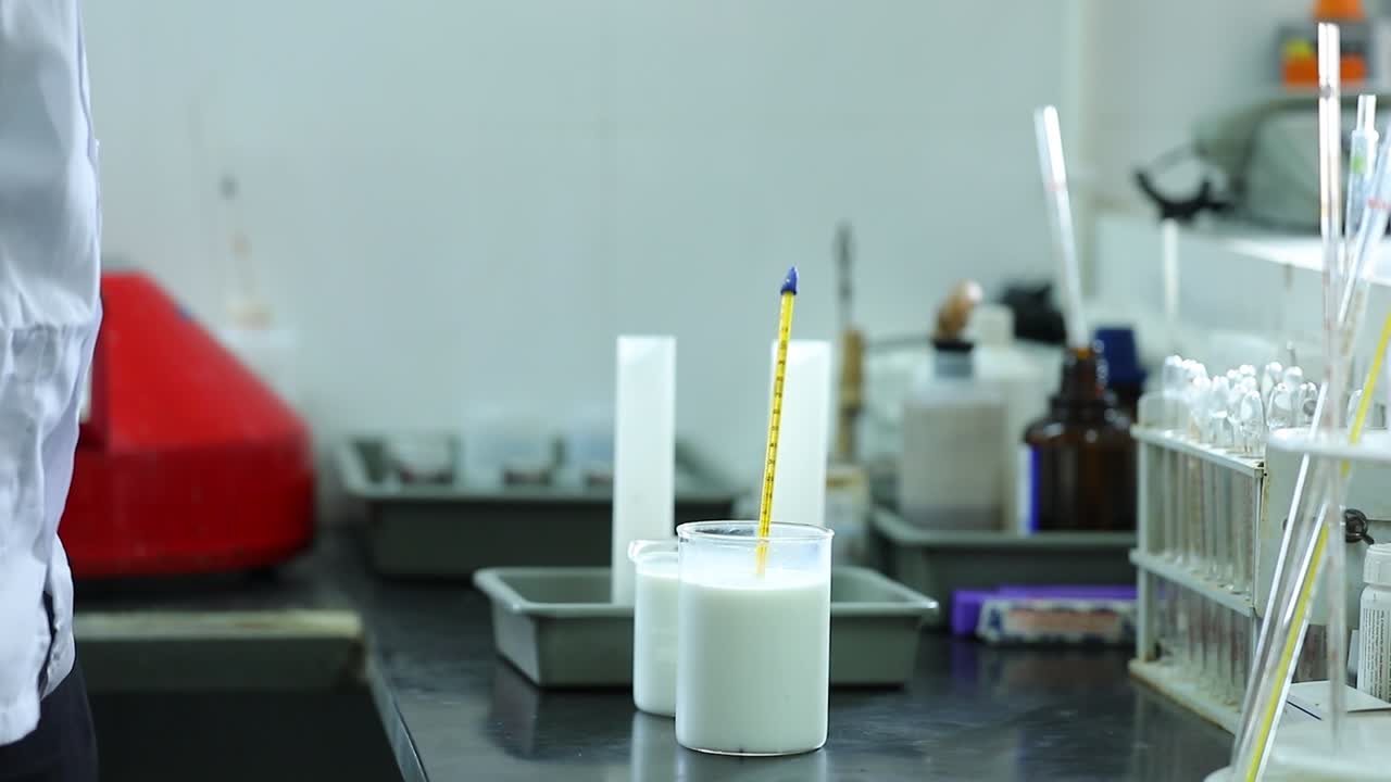 Professional expert with glass bottle of milk on blurred dairy equipment background. Dairy product concept
