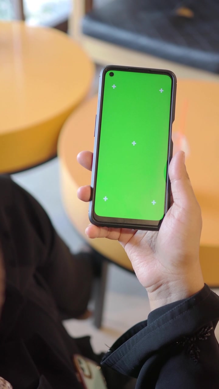 Persona con uno smartphone con schermo verde in un caffè