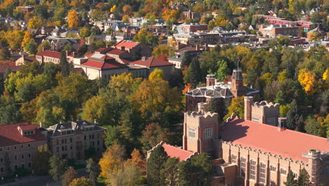 aerial up close view of cu boulder campus surrounded by green and yellow fall trees with the rocky flatiron mountains in the background in the front range of colorado