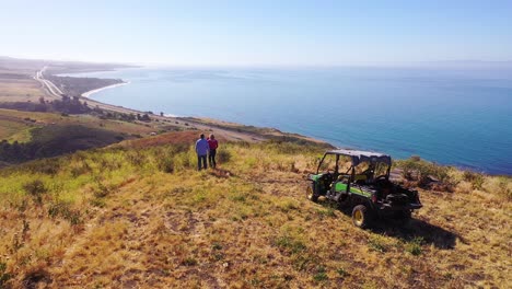 antena de un hombre y una mujer jubilados de pie junto a atv en la magnífica vista de la costa de la costa de gaviota, el océano pacífico y el condado de santa bárbara, california