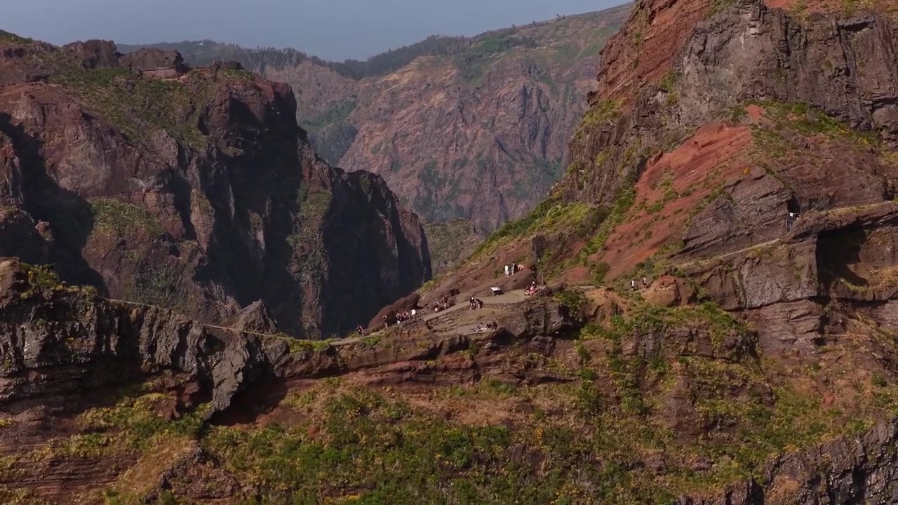 Ripresa con drone di turisti che fanno escursionismo e si riuniscono in un punto panoramico sulla cima di aspre vette montuose lungo il sentiero PR1 dell'isola di Madeira. Cielo limpido, colori vividi