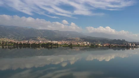 the town of paipa and its surrounding hills is reflected in lake sochagota, captured on a calm day with a 4k drone slowly moving left to right and gaining altitude