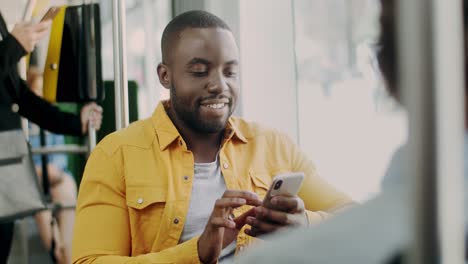 Retrato-Del-Joven-Guapo-Y-Alegre-Sonriendo-A-La-Cámara-Mientras-Se-Sienta-En-El-Tranvía-Y-Usa-El-Teléfono-Inteligente