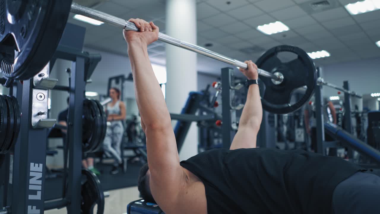 Close-up of heavy barbell in man's hands during workout. Muscular athlete lifting barbell up to build his arms muscles in sports club.