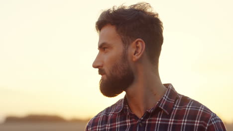 close up of the handsome man with beard turning to the camera and smiling in the field at the dawn