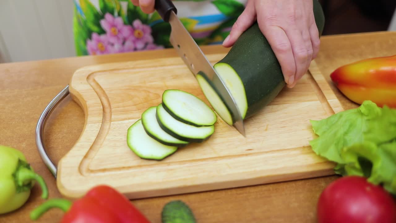 Women's hands Housewives cut with a knife fresh zucchini on the cutting Board of the kitchen table