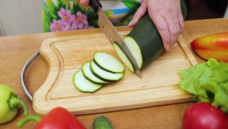 Frauenhände-Hausfrauen-Schneiden-Mit-Einem-Messer-Frische-Zucchini-Auf-Dem-Schneidebrett-Des-Küchentisches