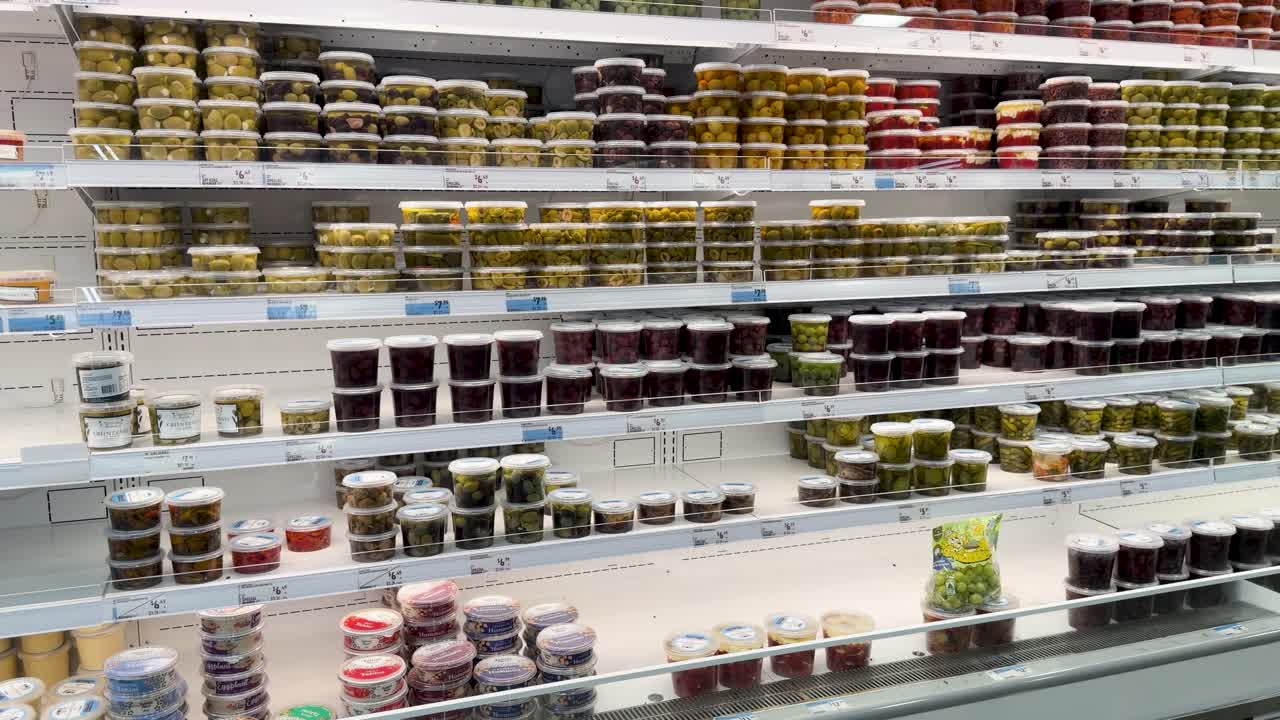 Um travelling lento pelas prateleiras refrigeradas de um supermercado, cheias de vários potes de comida embalada