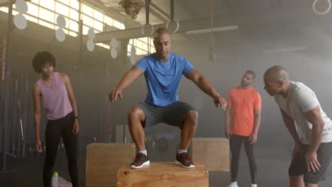 diverse group fitness class watching male coach jump onto box, cross training at gym, in slow motion