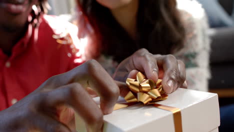 happy diverse couple putting bow on christmas gifts and embracing, slow motion