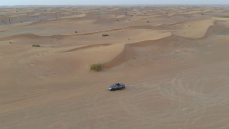 grey convertible car rides in the desert - distance drone shot including epic dunes and sky